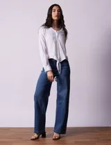 Blusa blanca de algodón marca Dash, con escote en V, abertura con botones, mangas 3/4 regulables con presilla y botón, y terminación de ruedo anudado.