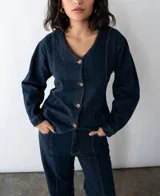 Camisa entallada de denim azul oscuro con cuello en V y cierre frontal con botones. Confeccionada en algodón reciclado con espalda ajustable.