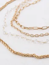 Collar dorado de tres cadenas con diferentes diseños: una de eslabones gruesos, una con cuentas de cristal y una con eslabones rectangulares.