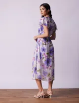 Vestido midi de gasa estampada con flores violetas y verdes, escote en V, abertura central con botones, cintura con lazo de ajuste y forro interno a tono.