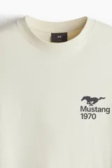 Remera color crema de corte holgado con estampado de un caballo Mustang y el año 1970 en el pecho. Cuello redondo con ribete fino y hombros caídos.