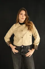 Chaqueta corta color beige con botones dorados, cuello redondo y puños marrones en contraste.
