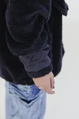 Canguro negro de polar con cierre de cremallera parcial, cuello alto y mangas largas con puños de tela lisa. Tiene un bolsillo tipo canguro con el logo de la marca bordado en el frente.