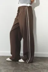 Pantalón de tiro alto negro a rayas verticales blancas, con cintura elástica ajustable con cordones, bolsillos delanteros y banda lateral blanca.