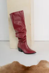 Bota alta de cuero color bordó, estilo bucanera, con caña fruncida y punta fina. Posee un taco bajo y ancho de color negro.