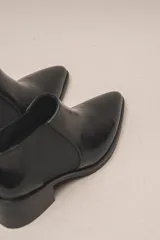 Botín negro de cuero vacuno con acabado charol, estilo botín Chelsea con puntera fina y elástico lateral. Posee un taco ancho y bajo de 5.5 cm.