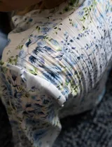 Blusa de gasa plisada estampada con flores azules, marca Floral & Ivy. Cuello a la base, escote en V y lazo de ajuste.