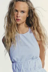 Top de popelina con rayas verticales celestes y blancas, cuello halter ajustable, detalle de frunces, espalda descubierta con tira ajustable y cierre lateral con cremallera oculta.