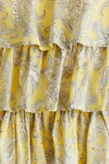 Vestido corto amarillo con estampado paisley, escote en V, breteles finos ajustables y falda escalonada con volados. Presenta un cierre oculto en la espalda y forro interior.
