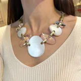 Collar corto con cordón gris, piezas ovaladas de resina blanca y transparente unidas por eslabones dorados.