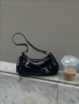 Cartera tipo baguette negra de cuero sintético con correa corta y detalles de hebillas plateadas.