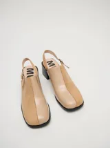Mocasines color beige con taco bloque de madera color negro y correa trasera ajustable.