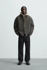 Sobrecamisa de hombre con corte relaxed fit, confeccionada en tejido de algodón acolchado con estampado a cuadros en tonos marrón, negro y beige. Tiene cuello solapa, manga larga con puños abotonados, bolsillo tipo parche en el pecho, aberturas laterales en el bajo y cierre frontal con botones a presión.
