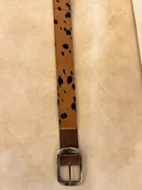 Cinturón de cuero con estampado animal print de vaca, hebilla metálica dorada y reverso de cuero color bordó.