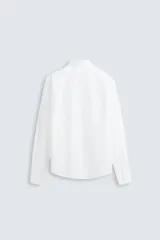 Camisa blanca de corte regular fit confeccionada en popelín de algodón. Tiene cuello abotonado, manga larga con puños abotonados y cierre frontal con botones.