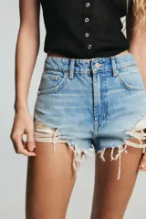 Short de jean de tiro alto, color celeste claro desgastado, con roturas grandes y deshilachado en el bajo. Presenta cinco bolsillos y cierre frontal con botón metálico.