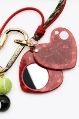 Llavero metálico con mosquetón dorado y charms colgantes desmontables: corazón rojo con espejo interior, llave, pelota de tenis, tiburón azul y bola de billar número 8.