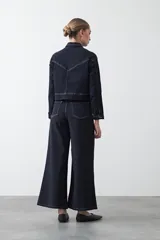 Pantalón de denim azul oscuro con corte flare, ajustado en la cadera y amplio en el ruedo. Presenta pespuntes a contratono en color blanco que resaltan las costuras.