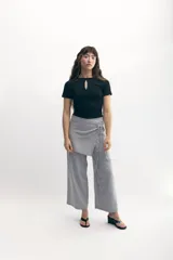 Pantalón palazzo gris con sobrefalda asimétrica atada a la cintura.