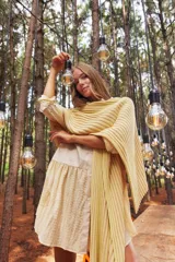 Ruana tejida color amarillo con rayas verticales en tonos rosados.