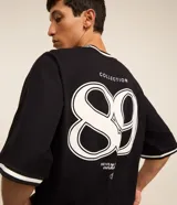 Remera deportiva negra de manga corta con cuello redondo y estampa frontal en relieve con la frase "Alternate Dept Collection Revealing the unknown Powered by Dreamerland".