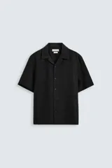 Camisa negra relaxed fit confeccionada en tejido de lino. Tiene cuello bowling, manga corta, bajo con aberturas laterales y cierre frontal de botonadura.