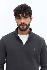 Buzo de algodón color verde musgo, con cuello alto y cierre frontal parcial. Presenta puños y cintura acanalados, y un pequeño logo bordado en el pecho.