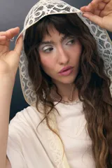 Capucha de encaje color crema con patrón circular, ribeteada en tono beige.