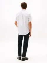 Camisa blanca a rayas verticales celestes, de corte clásico, manga corta, cuello abotonado y bolsillo en el pecho. Logo de Tommy Hilfiger bordado en el bolsillo.