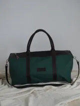 Bolso de lona color verde militar con detalles en cuero marrón. Tiene doble asa de mano y correa de hombro ajustable y extraíble.
