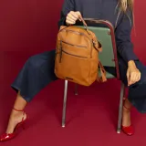 Mochila color beige de símil cuero con doble apertura superior con cierre. Incluye dos bolsillos al frente con cierres metálicos, asa rígida de mano y correa de galón. En la espalda correas de galón regulables.