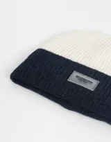 Gorro de lana tejido bicolor, blanco y azul marino, con etiqueta de goma con logo en el frente.