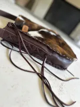 Bolso maxi de cuero con estampado de vaca en blanco y negro, y cuero color chocolate en la parte posterior. Tiene correa larga para colgar al hombro.