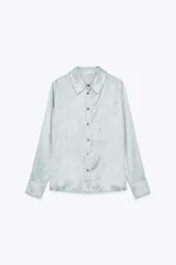 Camisa celeste de tejido satinado, con cuello solapa, manga larga con puños y cierre frontal con botones.
