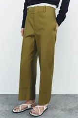 Pantalón color beige de corte ancho, con tiro medio, trabillas en la cintura y raya planchada.
