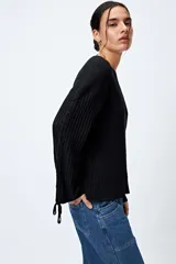 Sweater negro de punto canalé con detalle de trenzado en las mangas y lazo ajustable en el ruedo.