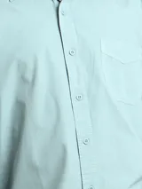 Camisa de manga larga color verde oliva, confeccionada en algodón. Tiene corte clásico, bolsillo en el lado izquierdo del pecho y cierre con botones.