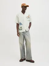 Camisa de algodón color crudo con estampado de flores y billetes, cuello resort, calce relajado, mangas cortas y cierre de botones.