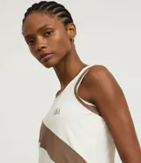 Musculosa deportiva de mujer, color blanco y marrón, con diseño de recortes diagonales y ribetes en contraste. Presenta un pequeño logo bordado en el pecho.