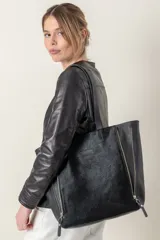 Bolso tote negro confeccionado en cuero vacuno con textura de pelo. Tiene doble asa de hombro y dos cierres metálicos laterales que permiten modificar su forma.