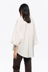 Camisa blanca de corte ancho y silueta relajada, con cuello camisero, botones frontales, manga 3/4 ancha con puño y bolsillo de plastrón en el pecho.