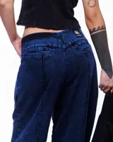 Pantalón de denim azul intenso, corte sastrero de pierna ancha, tiro alto o a la cadera (según el talle elegido), cierre frontal invisible, pretina cruzada y bordado negro del logo Temblad en la parte trasera.