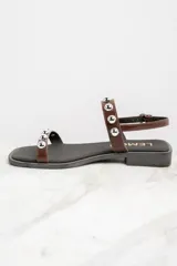 Sandalias bajas de cuero color marrón con apliques de tachas metálicas plateadas.