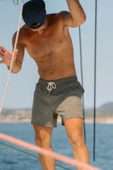 Short de baño para hombre color verde oliva con estampado de palmeras en blanco. Tiene elástico en la cintura, cordón ajustable, tres bolsillos (dos laterales y uno trasero), tela con 10% spandex de secado rápido y mesh hipoalergénico en el interior.