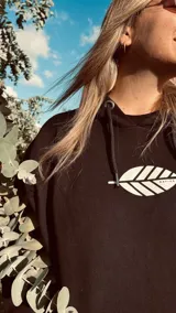 Hoodie negro de corte oversize con cordones ajustables y estampado frontal de una hoja blanca.
