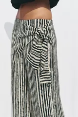 Pantalón de tiro alto con nudo delantero, de pernera ancha y estampado a rayas verticales en blanco y negro.