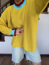 Sweater amarillo de tejido de punto, con cuello redondo con terminación en volados color borgoña y celeste, y puños con terminación en volados color borgoña y celeste.