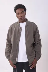 Campera bomber color marrón topo, con cierre frontal y bolsillos laterales con cierre. Tiene un bolsillo con cierre y etiqueta en la manga izquierda.