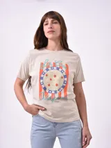 Remera blanca de algodón con cuello redondo y manga corta. Presenta un pequeño bordado en el pecho izquierdo con una figura que parece ser una persona acostada en una tabla de surf o flotador.