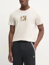Remera color crema de algodón regenerado, con cuello redondo y logotipo de Calvin Klein en un recuadro color ocre.